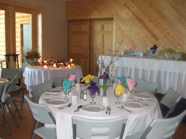 A round table set with white linen and coloured napkins in a pine-panelled room, with a candle-lit head table behind