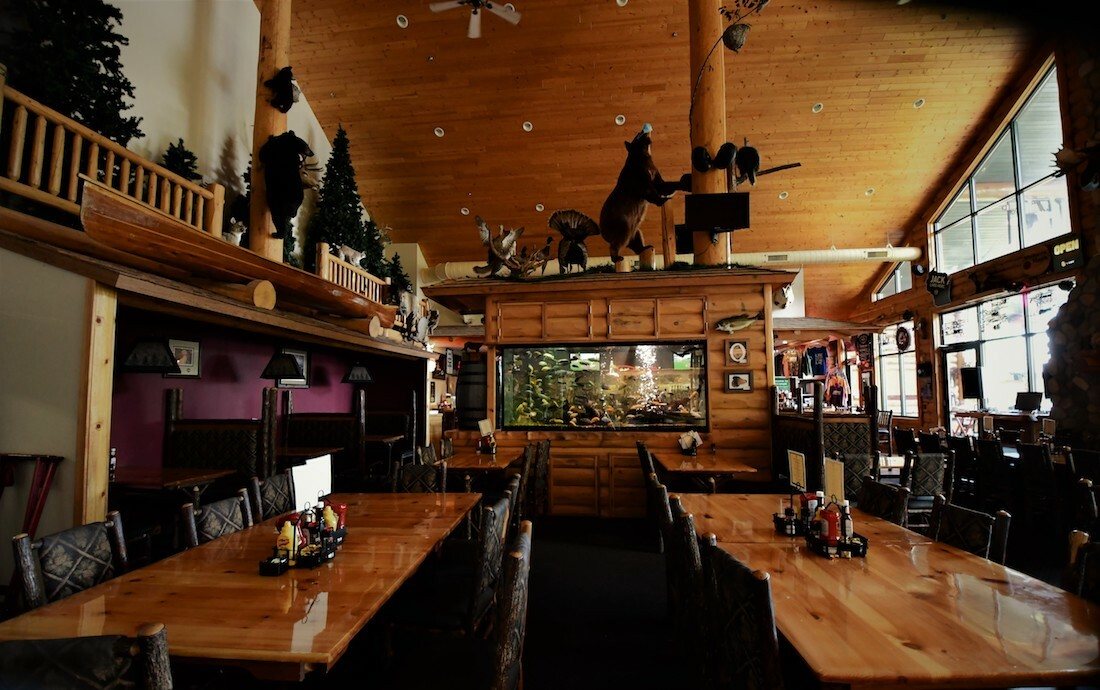 The log dining room with a vaulted pine ceiling, long pine tables, hickory chairs, mounted game and a built-in aquarium