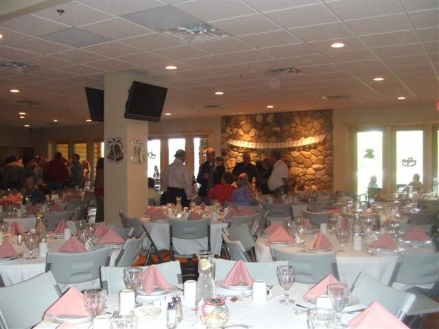The banquet hall set for a reception, round tables in white linen in front of a tall river-stone fireplace