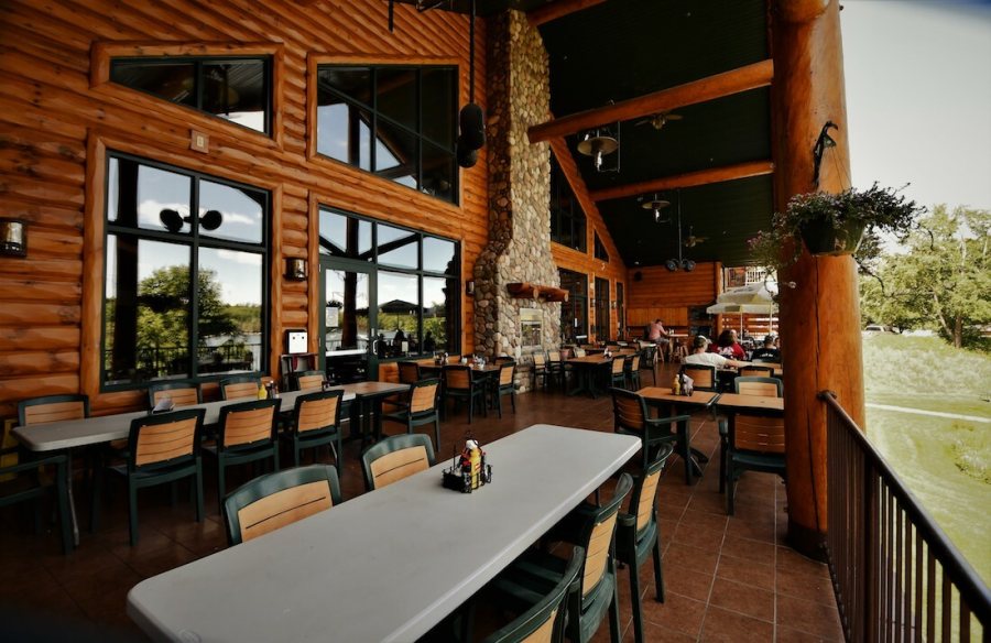 The enclosed lakeside dining porch, with a full-height river-stone chimney, log columns and windows onto the water