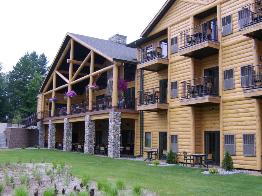 The three-storey log lodge seen from the lawn, with balconies and hanging flower baskets above a covered stone-pillared patio