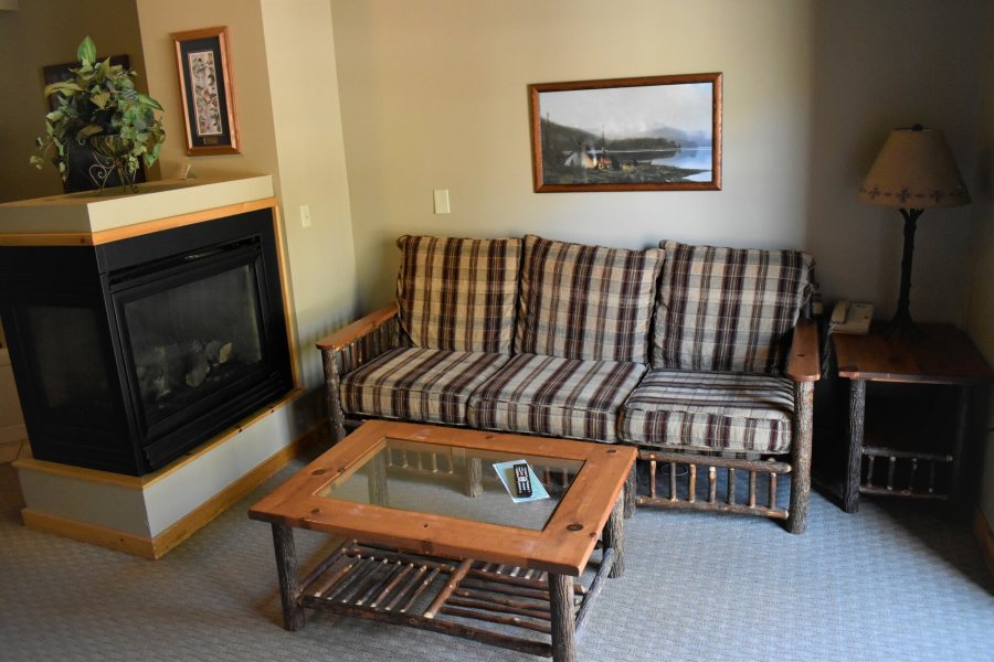 A suite sitting room with a gas fireplace, a plaid hickory-log sofa and a glass-topped log coffee table