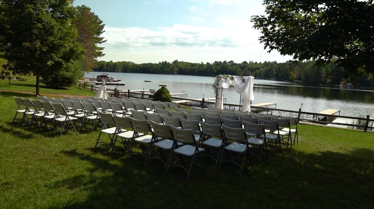 Rows of white chairs set out on the lawn facing a flower-draped arch, with the docks and Waubee Lake behind