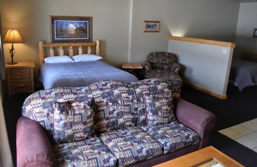 A lodge suite with a log-frame bed, a patterned sofa bed and a second bed on a raised level behind a half wall